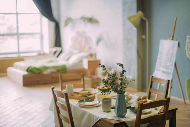 Σύγχρονη κουζίνα σε σκανδιναβικό ρουστίκ στυλ με ανοιχτόχρωμες πράσινες αποχρώσεις. Κουζίνα και τραπεζαρία λεπτομέρειες τραπέζι με πρωινό σερβίρεται σε κεραμικά πιάτα - Φωτογραφία, εικόνα