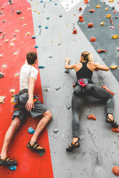 couple of athletes climber moving up on steep rock, climbing on artificial wall indoors. Extreme sports and bouldering concept - Foto, imagen