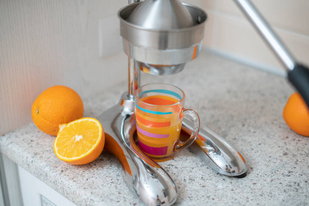 steel metal manual press juicer with cut oranges and glass on the kitchen table at home - Photo, Image