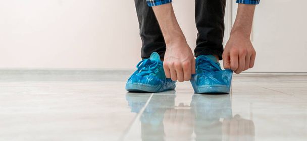 τα πρόσωπα χέρια που τίθενται στα μπλε καλύμματα παπουτσιών στα βρώμικα αθλητικά παπούτσια στο νοσοκομείο - Φωτογραφία, εικόνα