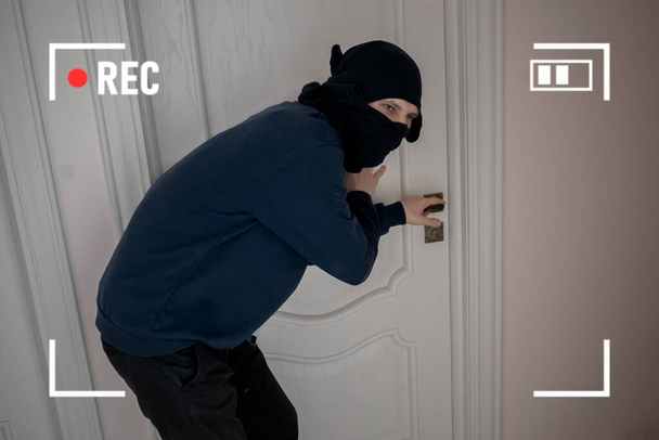lupič zločinu v černé masce se snaží vylomit dveře na dům bytů, tajný kamerový systém cctv - Fotografie, Obrázek