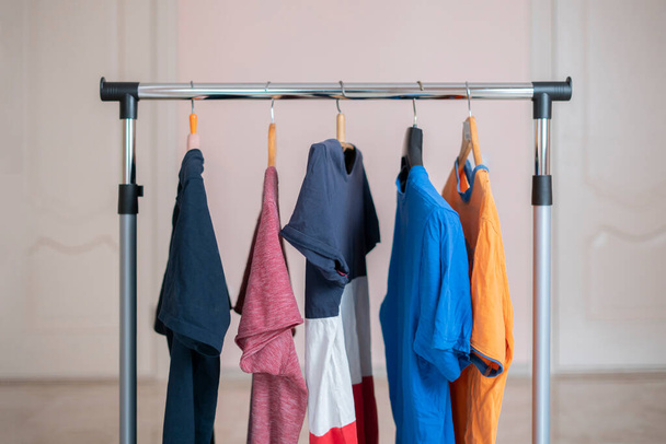 um conjunto simples de camisetas coloridas em um cabide em casa perto da parede, conceito minimalista simples - Foto, Imagem
