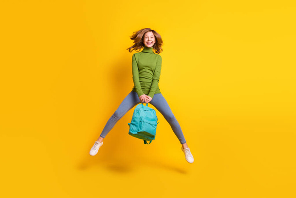 Full length body size photo girl jumping up wearing backpack smiling isolated vibrant yellow color background - Photo, image