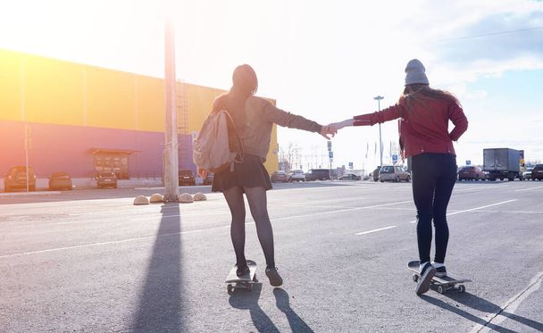Une jeune fille hipster fait du skateboard. Filles copines pour une promenade en ville avec un skateboard. Sports de printemps dans la rue avec une planche à roulettes
 - Photo, image