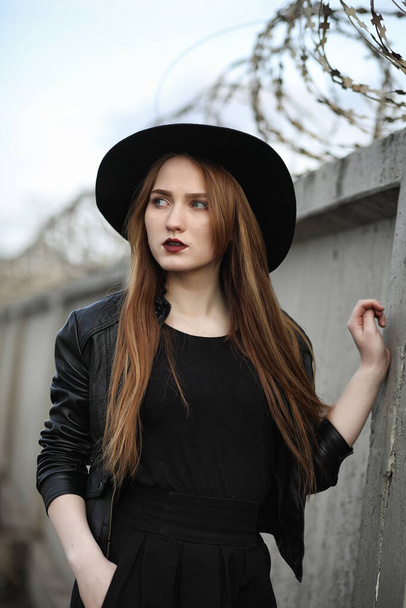 Young beautiful girl in a hat and with a dark make-up outside. Girl in the Gothic style on the street. A girl walks down the city street in a leather waistcoat with phone - Foto, Imagem