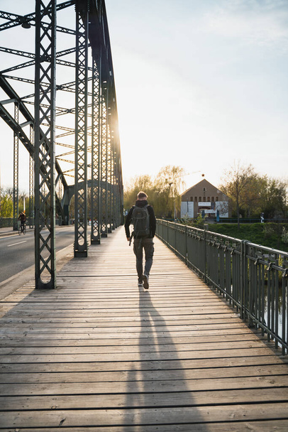 A young tourist with a backpack walking alone on a wooden bridge during the sunset - Fotografie, Obrázek