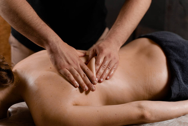 Attractive girl is relaxing on classic massage procedure in spa. Manual therapy. Masseur is doing back massage - Foto, immagini