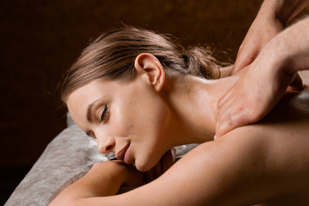 Attractive girl is relaxing on classic massage procedure in spa. Manual therapy. Masseur is doing shoulder massage - Foto, Imagem