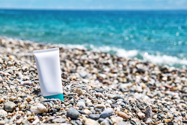 Botella de crema solar en la playa de arena junto al mar. SPF protector solar concepto de protección. Cosmética natural - Foto, Imagen
