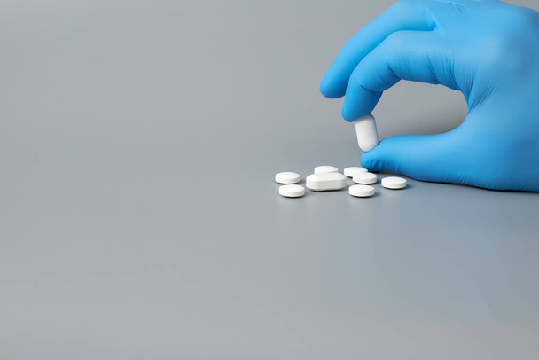 A gloved hand holds a white pill on a gray background - Photo, image