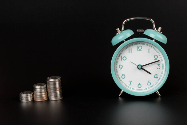 Business metafora käsite aika on rahaa käsite. Sininen herätyskello ja kolikot mustalla pohjalla - Valokuva, kuva