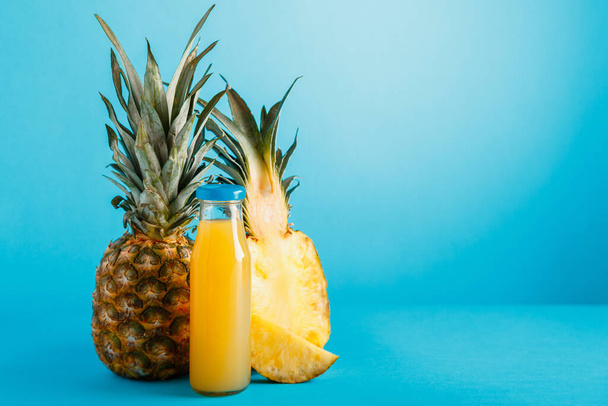 Tasty pineapple juice in glass bottle with ingredients on Blue color summer background with copy space. Fresh natural pineapple cocktail, pineapple juice in glass bottle. - Photo, image