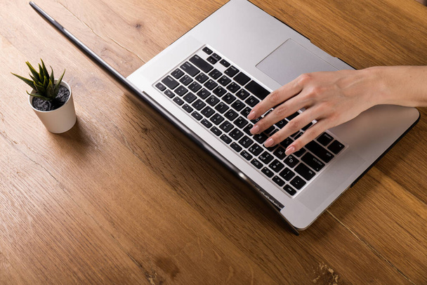 Femme travaillant avec un ordinateur portable sur une vieille table en bois. Mélange de fournitures de bureau et de gadgets sur un fond de bureau en bois. espace de copie. - Photo, image