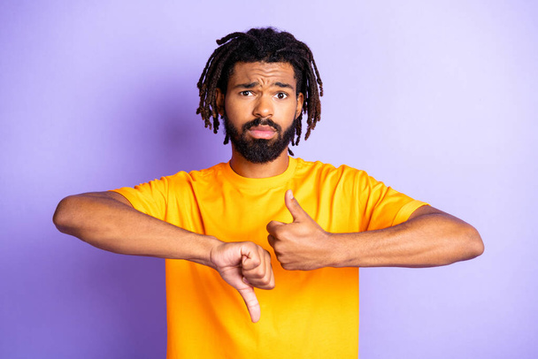 Portret van mooie trieste brunette kapsel guy show duim naar beneden dragen oranje t-shirt geïsoleerd op lila kleur achtergrond - Foto, afbeelding