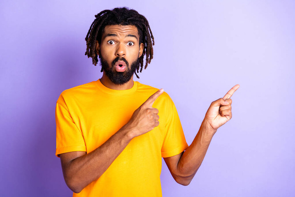Portrait of nice impressed brunet guy point empty space wear orange t-shirt isolated on vibrant lilac color background - Foto, afbeelding