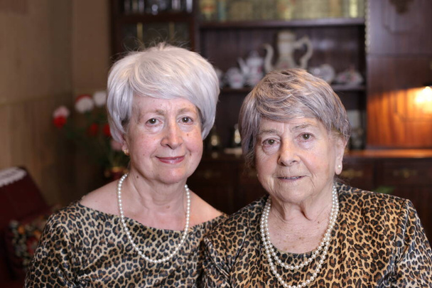 портрет двух зрелых женщин в стильных платьях с аксессуарами дома - Фото, изображение