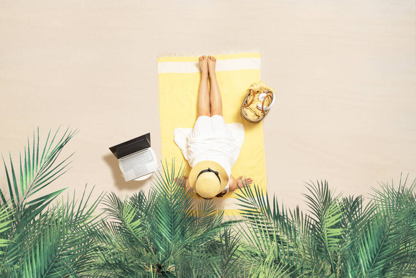 Woman with laptop, bag and headphones sitting on the beach towel and enjoying summer vacation under palm trees branches. Aerial view - Foto, Imagen
