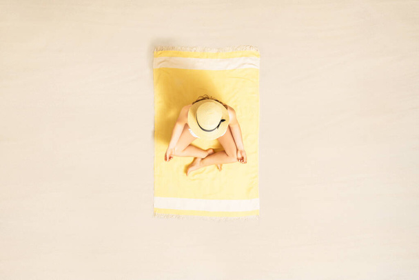 Woman in bikini meditates and relaxation in lotus pose sitting and sunbathing on yellow beach towel. Yoga. Summer vacation. Top, aerial view - Foto, Imagen