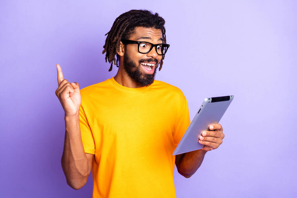 Portrait of nice impressed brunet guy type tablet finger up wear spectacles orange t-shirt isolated on vibrant lilac color background - 写真・画像