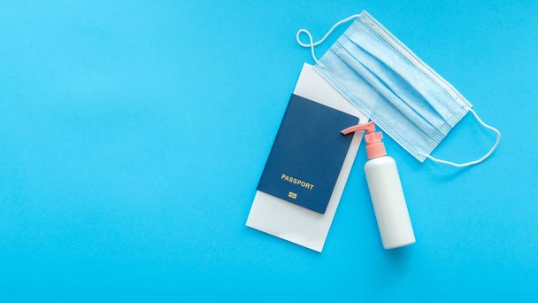Protective medical mask sanitizer and passport airplane ticket. Concept vacation safe travel flights during covid and coronavirus lockdown. Long web banner on color blue background with copy space.  - 写真・画像