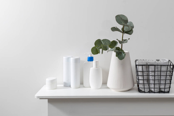 A vase with a eucalyptus branch, plastic bottles of shampoo, cream. Bathroom. Space for text. Metal basket with rolled face towels - Photo, image