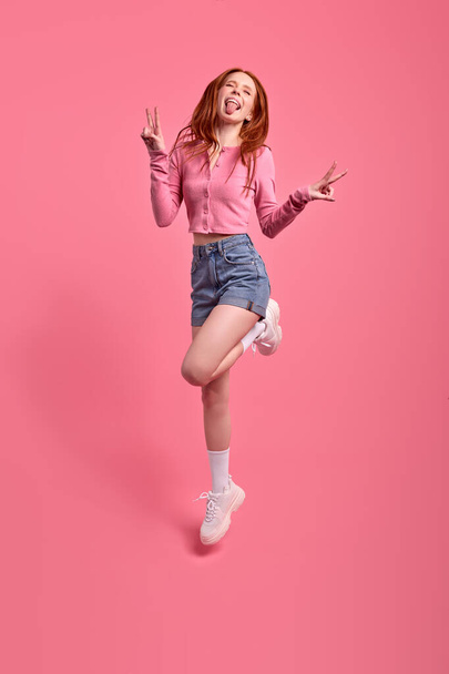 Full length portrait of Excited redhead woman jumping showing v-sign isolated - Valokuva, kuva