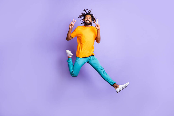 Full size photo of nice optimistic brunet guy jump show v-sign wear t-shirt pants isolated on lilac color background - Fotografie, Obrázek