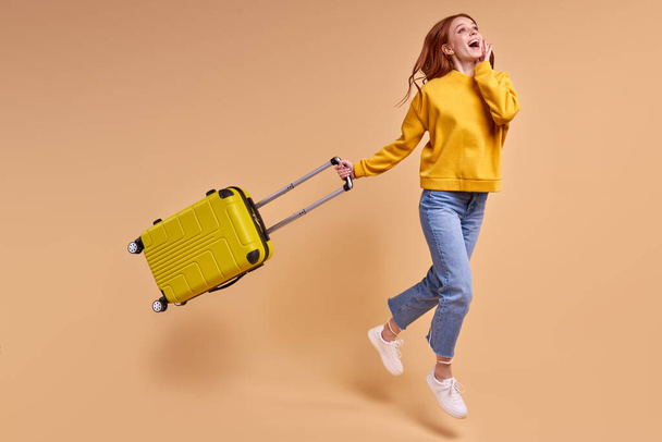 Traveler tourist redhead woman with suitcase, jumping in casual outfit isolated - Foto, Imagen
