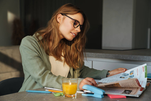 Орієнтована гарна студентка робить домашнє завдання, сидячи за столом вдома
 - Фото, зображення