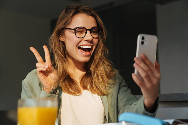 自宅で携帯電話で自慰行為をしながら平和サインを示す幸せな素敵な女性 - 写真・画像