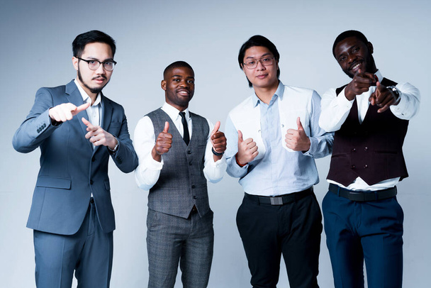 Groep van Afro-Amerikaanse en Aziatische zakenmannen in pakken wijzen vingers naar de camera en duimen omhoog - Foto, afbeelding