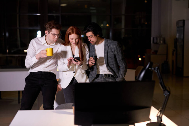 Young Caucasian Men And Woman Colleagues Having Rest After Work In Office, Use Smartphone - Foto, imagen