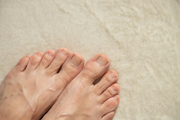 pies femeninos descalzos de pie sobre una alfombra blanca en casa, pies sobre un fondo blanco, pies femeninos - Foto, Imagen