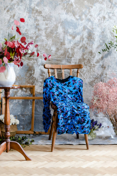 Old wooden chair with blue dress in studio room with flowers - Фото, изображение