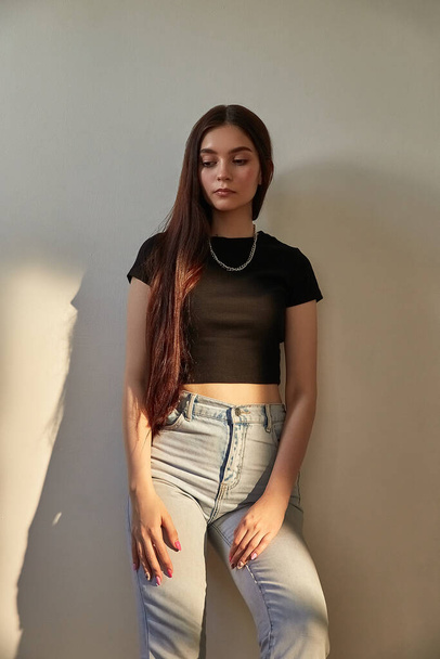 portrait of young caucasian girl with long hair in jeans standing next to wall - Photo, Image