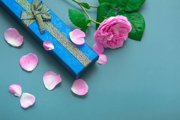 Draufsicht zum Vatertag auf blauem Hintergrund mit Rosenblättern. Nahaufnahme von Geschenk blaue Schachtel mit goldenen Schleifen und rosa Rose.  - Foto, Bild