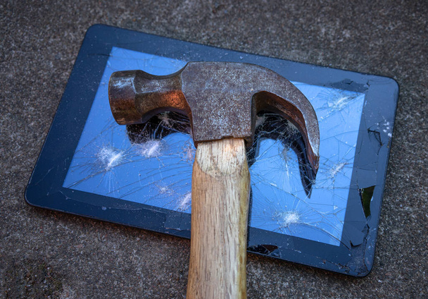 A metal hammer with a wooden handle lies on the broken display of a tablet computer - Foto, Bild