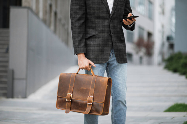 Close up of man holding suitcase and smartphone on street - Foto, Imagen