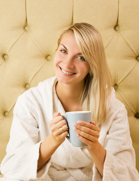 美しい若い女性がベッドの上に座ってコーヒーを飲むの - 写真・画像