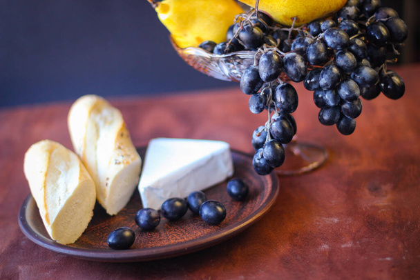 Maravillosa comida: cepillos de uva oscura, un trozo de queso brie, dos trozos de baguette y unas peras amarillas maduras - Foto, Imagen