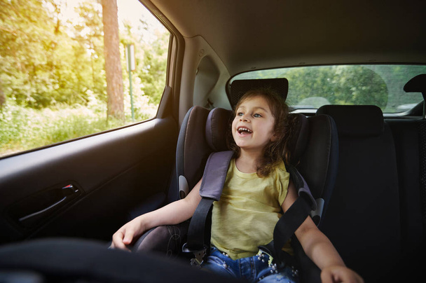 Mouvement sûr des enfants dans la voiture. Fille heureuse dans un siège auto enfant portant une ceinture de sécurité tout en voyageant en voiture - Photo, image