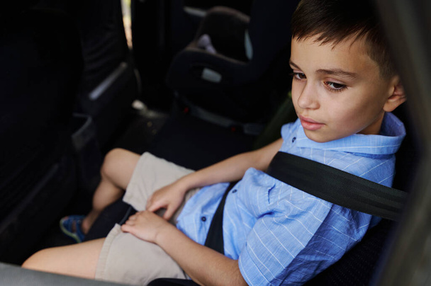 Ένας έφηβος που φοράει ζώνες ασφαλείας ταξιδεύει με το αυτοκίνητο σε ένα προστατευτικό παιδικό κάθισμα αυτοκινήτου. Ταξιδεύοντας με ασφάλεια με τα παιδιά. Ασφαλής μετακίνηση των παιδιών στο αυτοκίνητο - Φωτογραφία, εικόνα