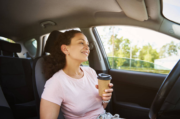 Young African American ethnicity woman enjoying coffee break in her car during stop - Photo, Image