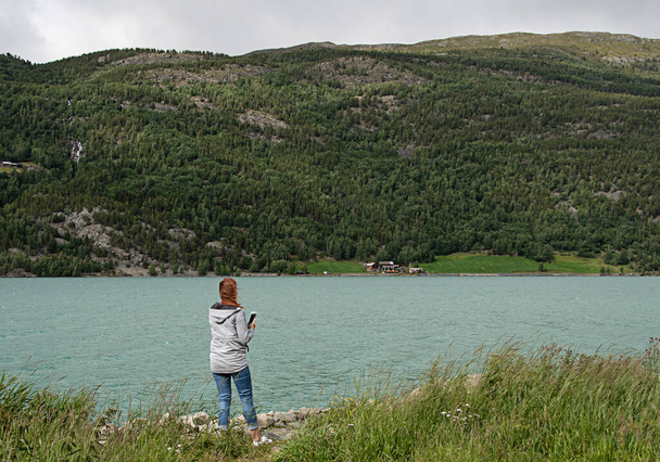 女性はターコイズブルーの湖を撮影する。色は山の融雪による藻によって引き起こされます。ノルウェーのVg. - 写真・画像
