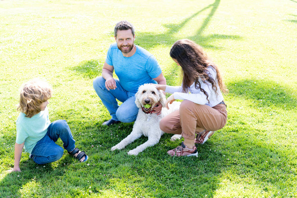 緑の公園の草の上の父親の母親と子供。ペットとの友好的な家族. - 写真・画像