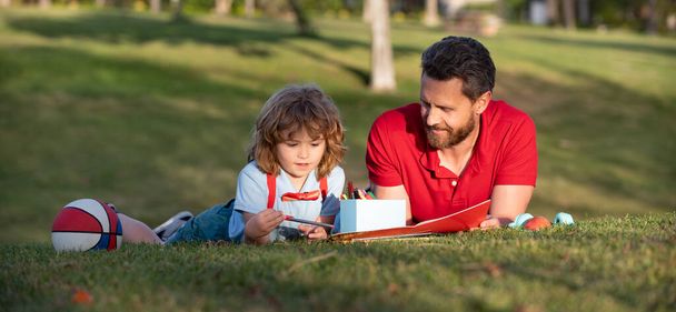 Vater und Sohn entspannen sich auf Gras im Park und lernen zeichnen - Foto, Bild