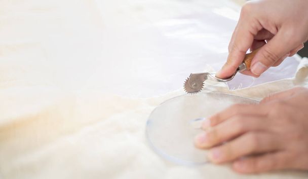 Крупный план стола портных с женскими руками, прослеживающими ткань с линейкой кривой для создания шаблона для одежды в мастерской-студии. - Фото, изображение