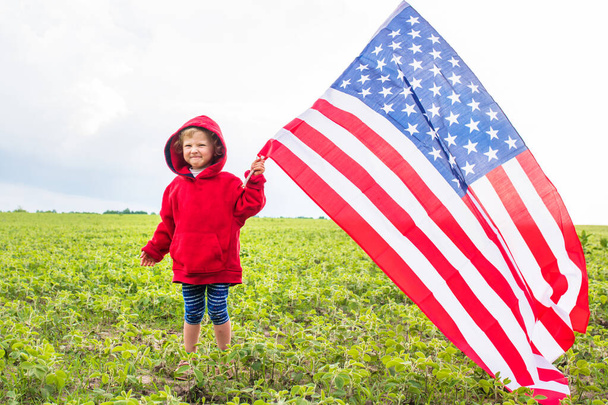 大豆の分野を背景に子供の手に米国の巨大な旗。アメリカは７月４日を祝う。独立記念日のコンセプト. - 写真・画像