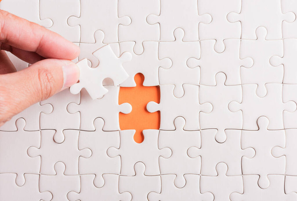 Top view flat lay of hand-holding last piece white paper jigsaw puzzle game last pieces put to place for solve problem complete mission, studio shot on an orange background, quiz calculation concept - Φωτογραφία, εικόνα