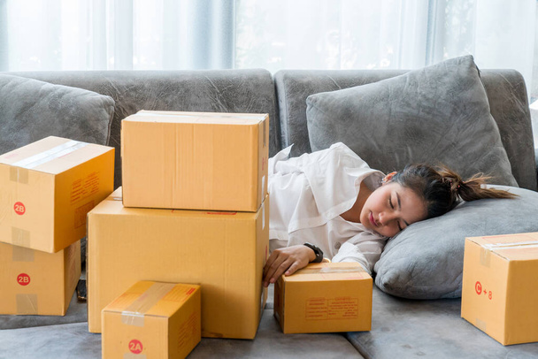 Hermosas mujeres asiáticas duermen en el sofá con muchas cajas de paquetes con pequeñas empresas venden al cliente en las compras en línea. - Foto, Imagen